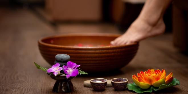 A person about to dip their foot into a bowl, accompanied by flowers and salts